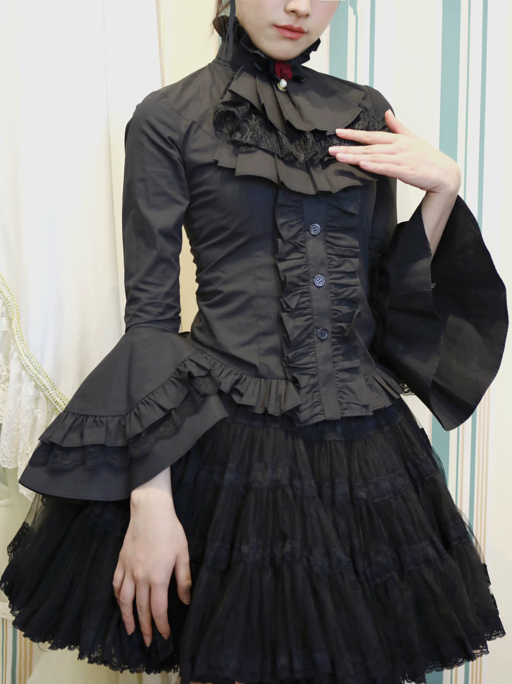 Black blouse with a high ruffled collar, front ruffles, lace trim and flared sleeves on a model.