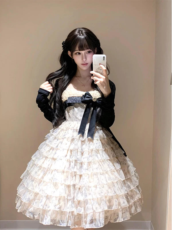 Model wearing a pale tiered JSK dress with a dark bow and long-sleeve cardigan.