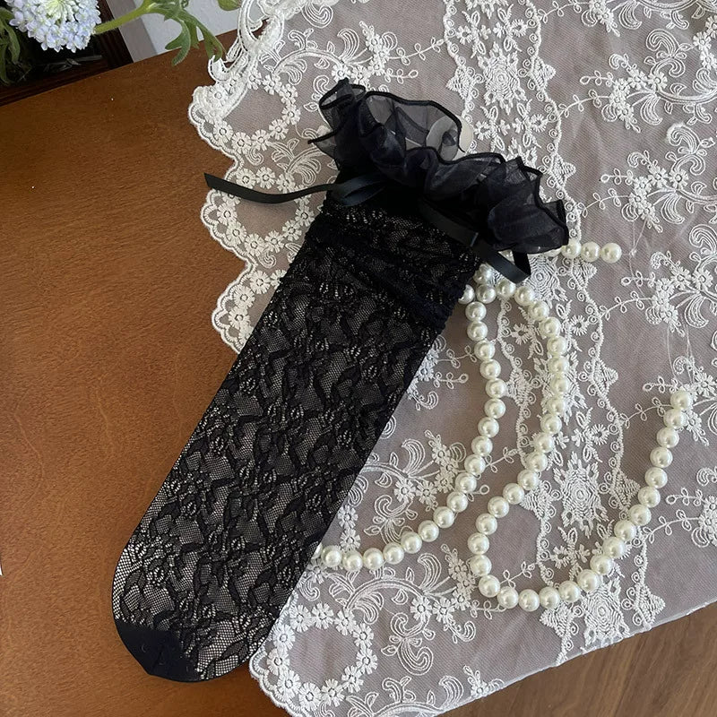 White lace-mesh mid-calf socks with ruffled tops and ribbon ties styled with white heels.