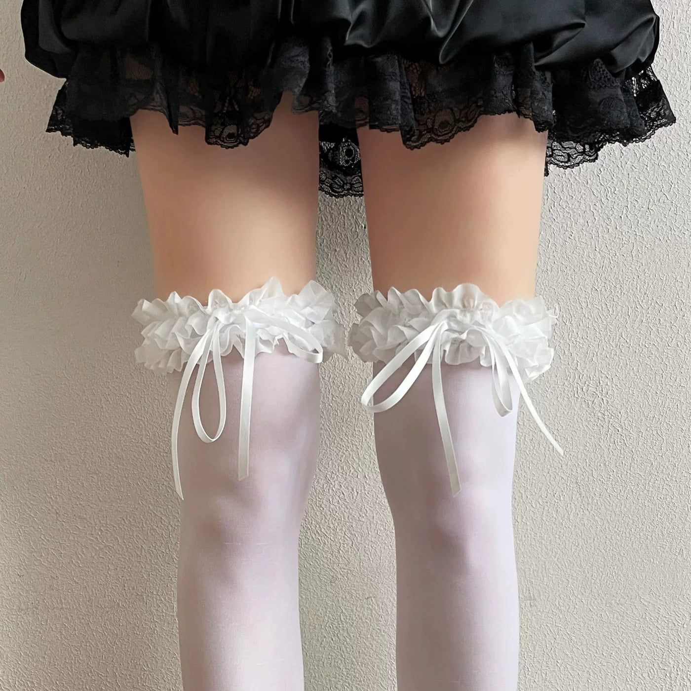 White thigh-high stockings with layered lace ruffles and long ribbon bows worn with an ivory Lolita outfit.