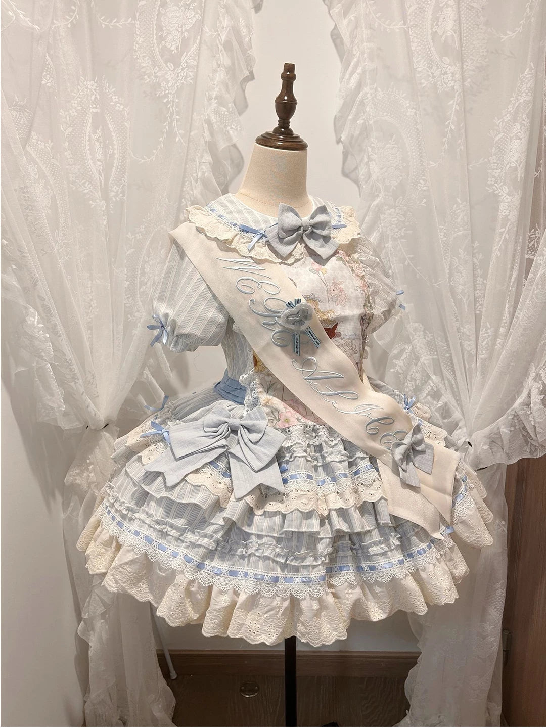 Water-blue OP dress on a mannequin with a sash, lace layers, and a printed chest panel.