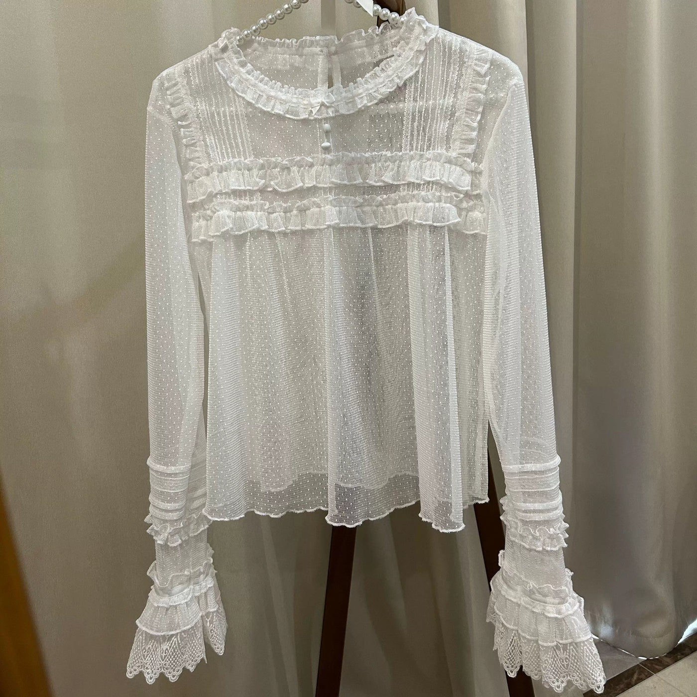 White sheer ruffle-trimmed long-sleeve inner top hanging on a pearl hanger.