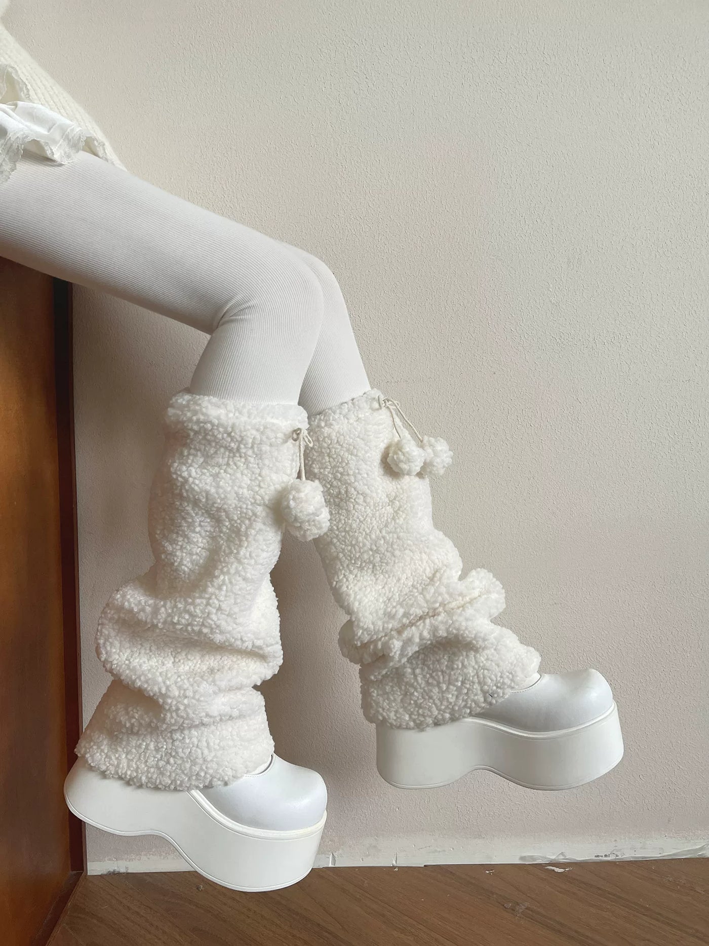 White fluffy-textured leg warmers with pompom ties styled over white tights.