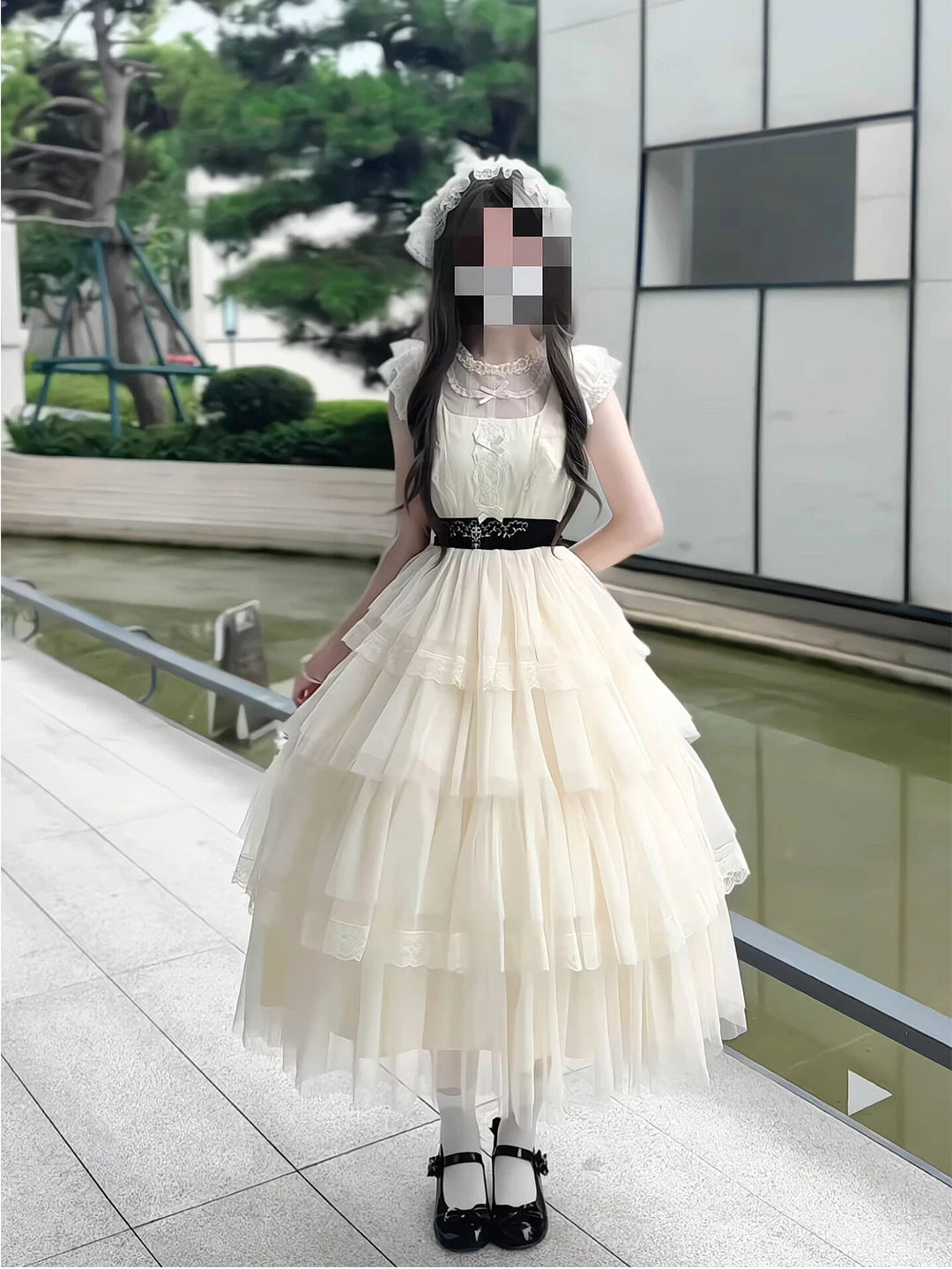 Cream lace one-piece dress with tiered full skirt and dark waist belt worn outdoors.