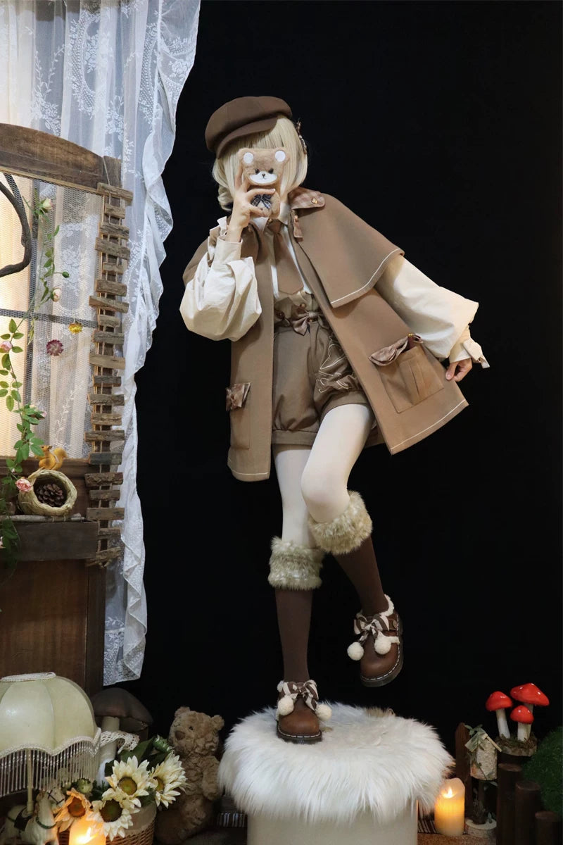 Model wearing a warm brown cape coat with white piping, bow-accented pockets and a cape overlay.
