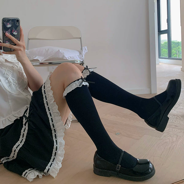 Black mid-calf socks with lace-trimmed cuffs and bow accents worn with a black dress