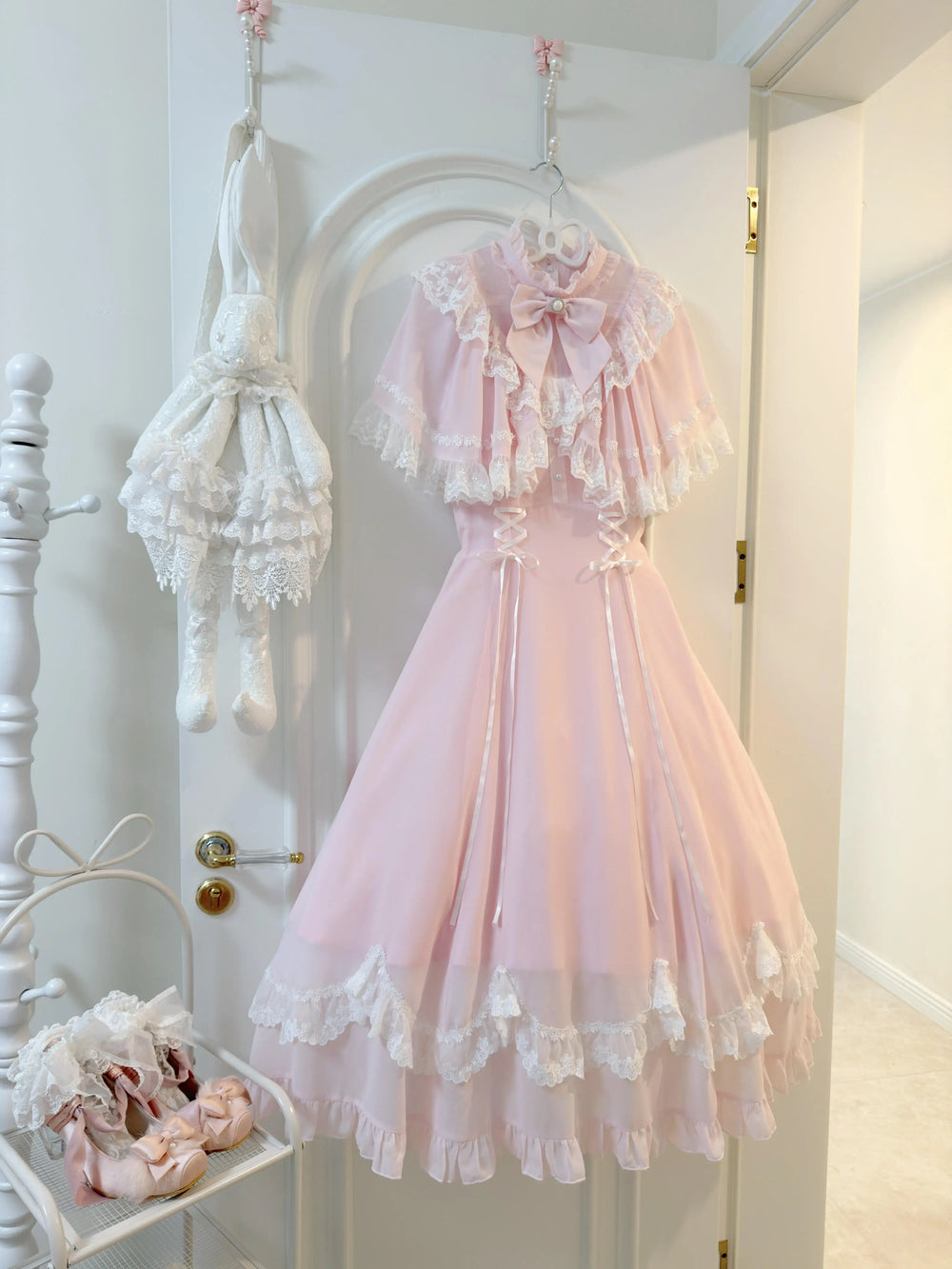 Pale pink lace capelet lolita dress with white trim and pearl bow, front view
