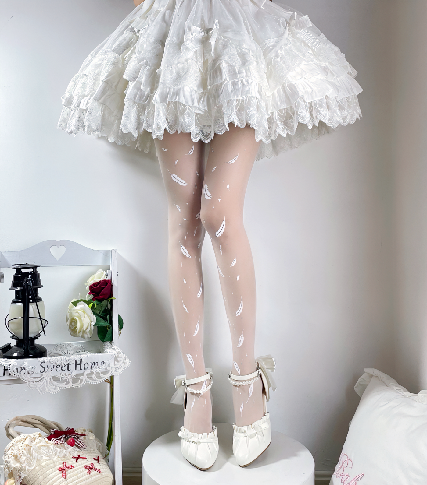 White tights with scattered feather and star motifs styled with white shoes beneath a ruffled skirt.