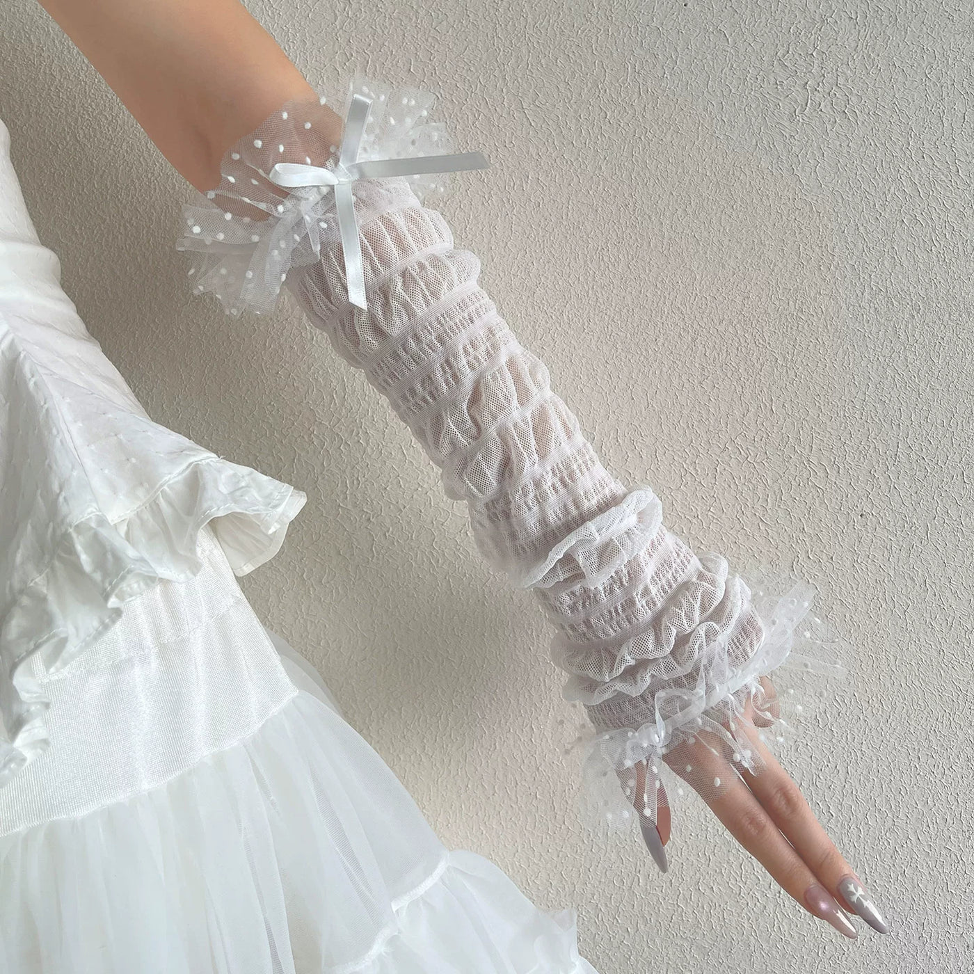 Model wearing white dotted mesh arm sleeves with ribbon bows and a white dress