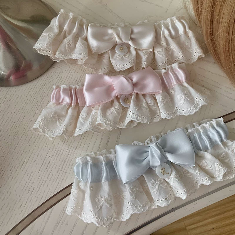 Three lace thigh garters in cream, pink and blue with bows arranged on a tabletop.