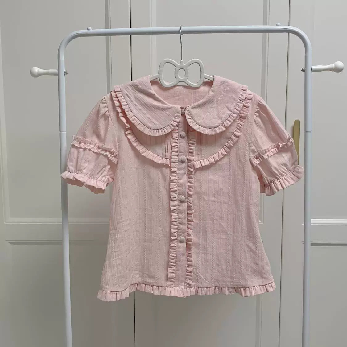 White and pink short-sleeve blouses with rounded ruffle-trimmed collars on a clothing rack