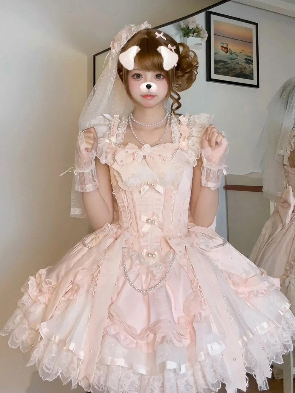 Model wearing a pale pink ruffled Lolita dress with pearl trim and matching headwear.