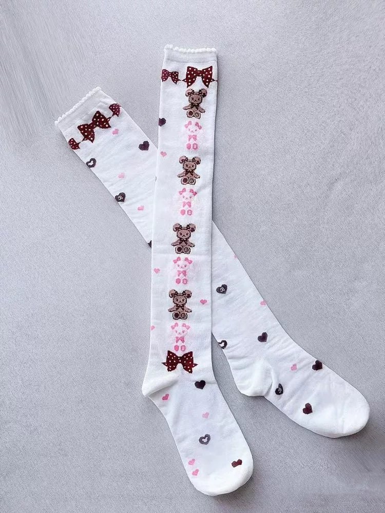 Off-white over-knee socks with teddy bears, pink bows and hearts worn with pink shoes.