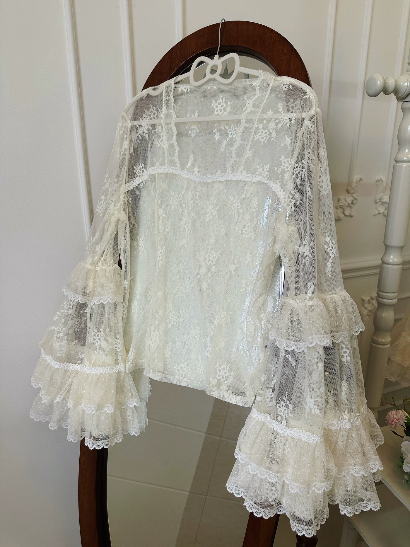 White lace-and-tulle long-sleeve inner top with tiered ruffle sleeves displayed on a hanger.