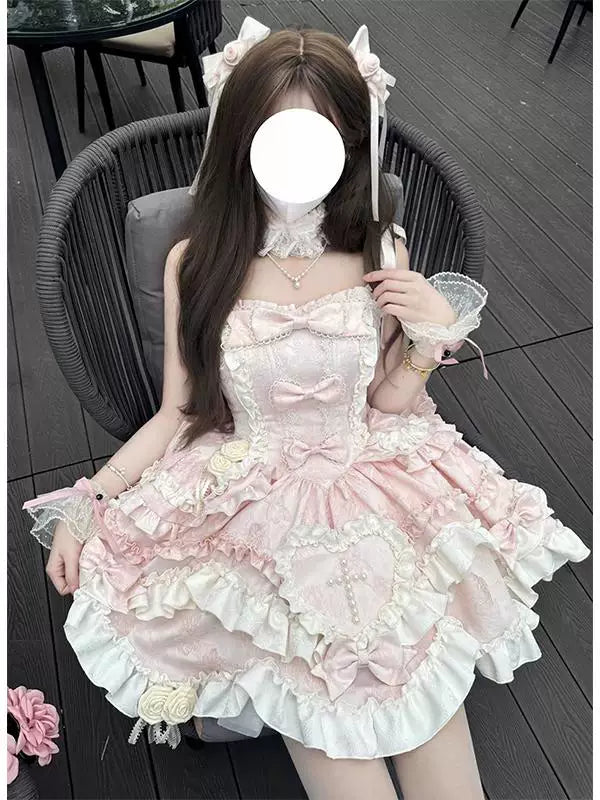 Pink and white ruffled JSK dress with bows and suspender straps styled on a seated model.