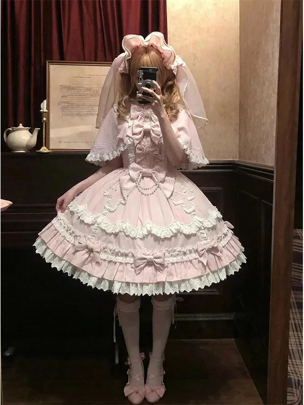 Pale pink JSK dress set with a cape, bows and layered skirt shown in a mirror.