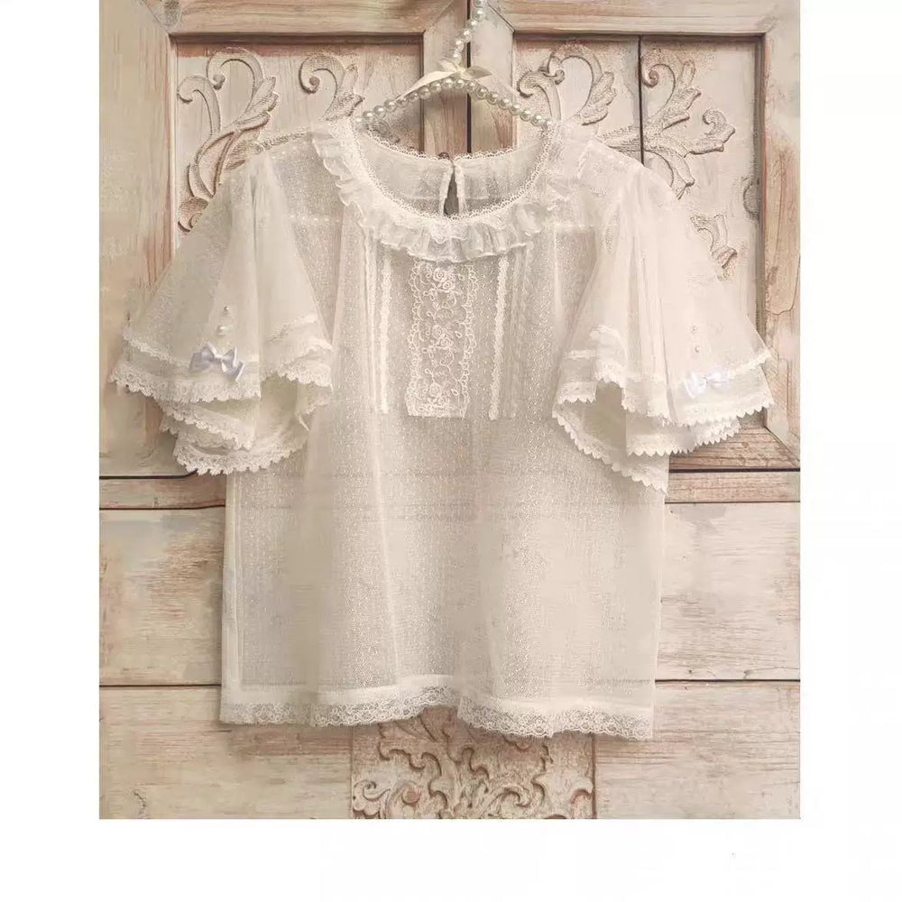 Off-white dotted-tulle inner blouse with lace trim and flutter sleeves hanging on a wooden hanger.
