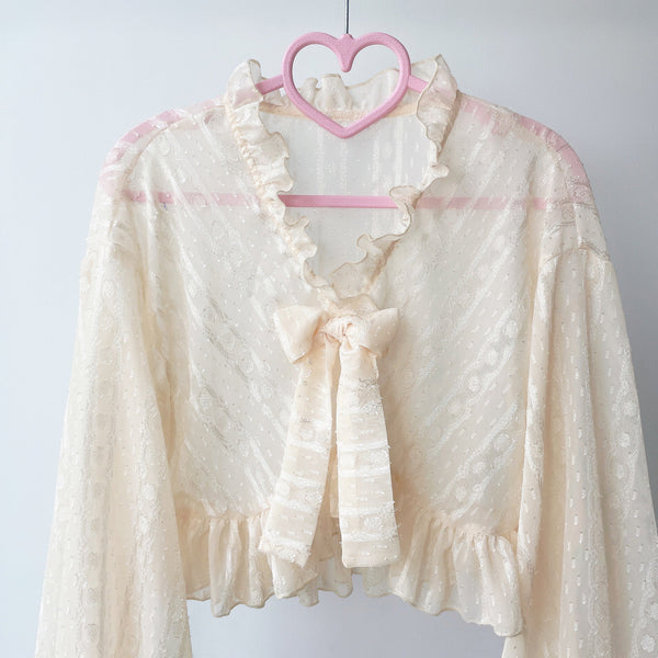 Ivory chiffon garment with a ruffled collar and bow, shown on a hanger.