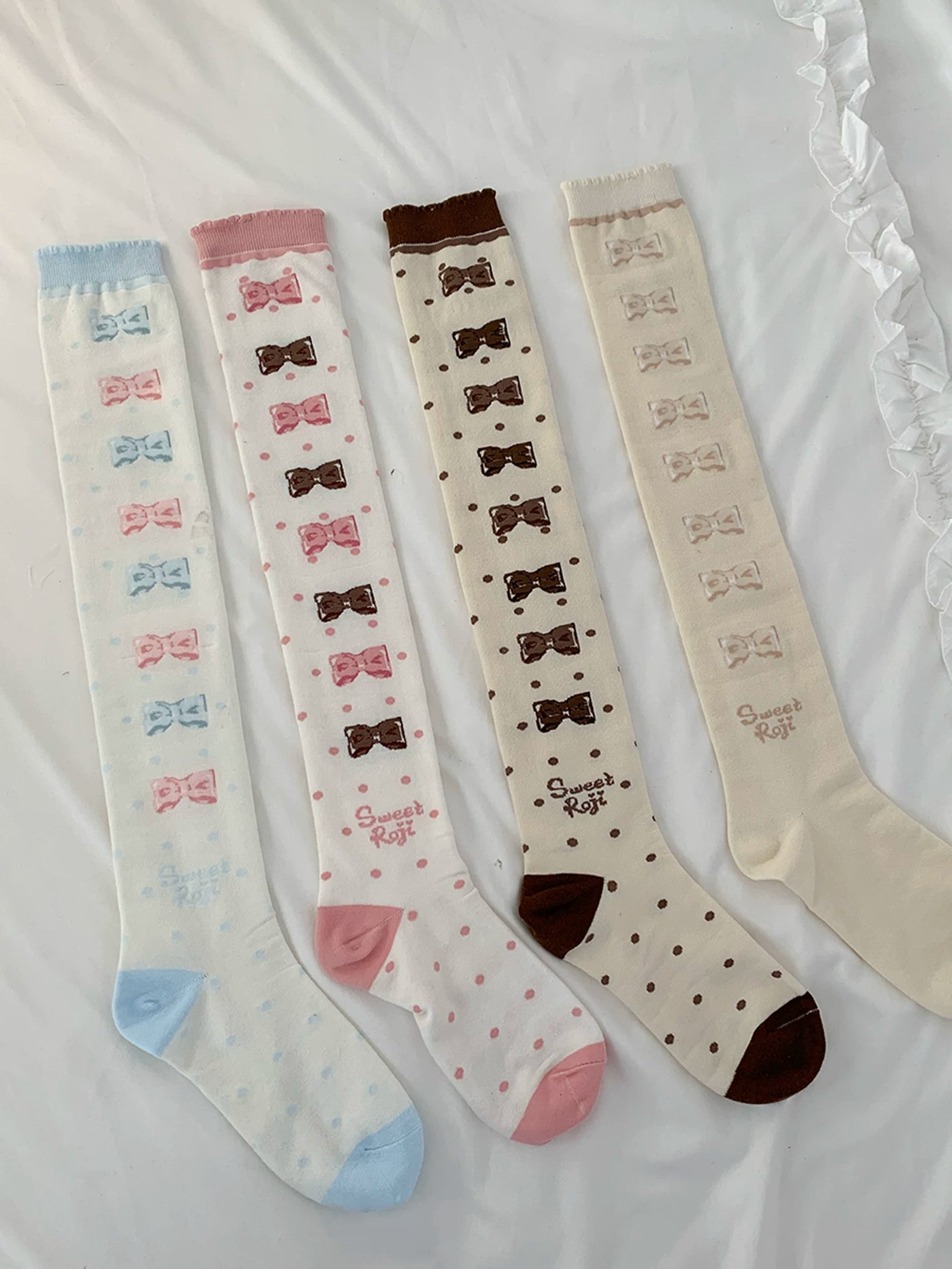 Four colourways of roji roji over-the-knee socks with bow and polka-dot motifs laid flat.