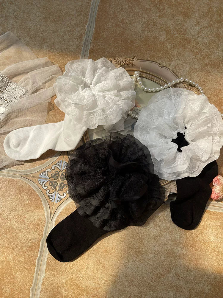 White and black layered lace ruffle socks arranged beside pearls and a decorative mirror
