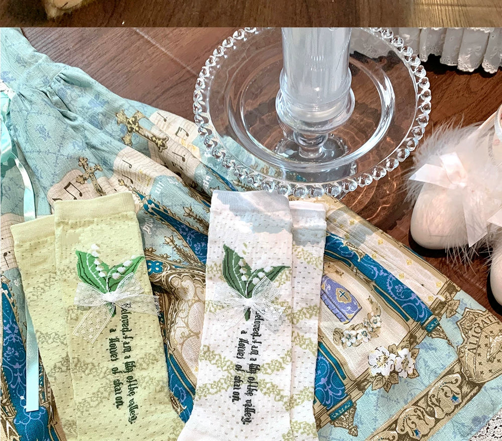 White and green lily-of-the-valley lace socks with bow details arranged on printed blue fabric.
