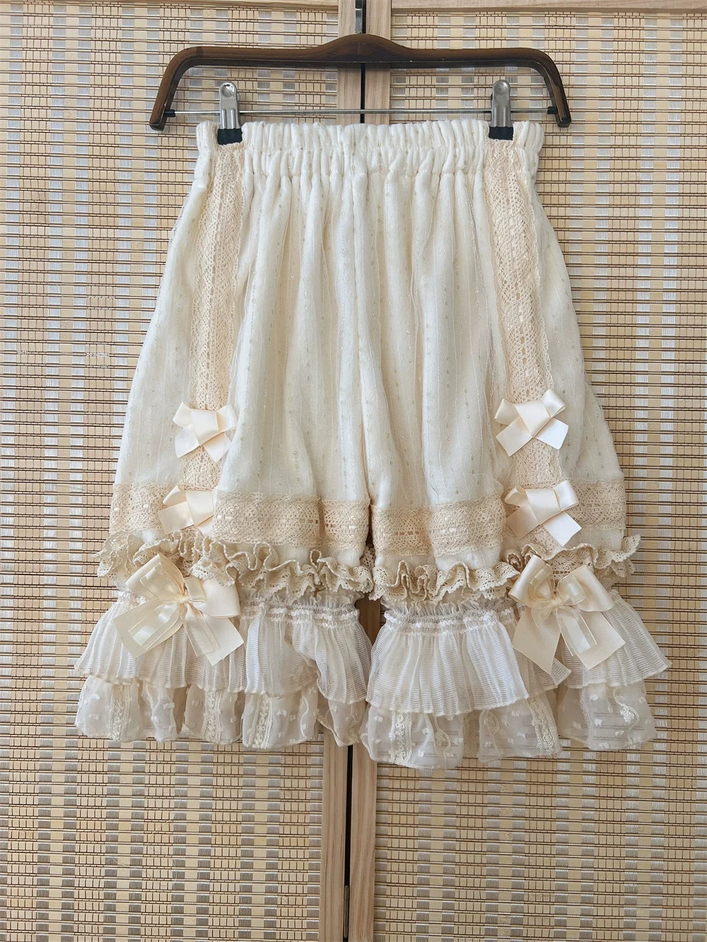 Creamy white Lolita bloomers with lace panels, bows and layered ruffle cuffs on a hanger