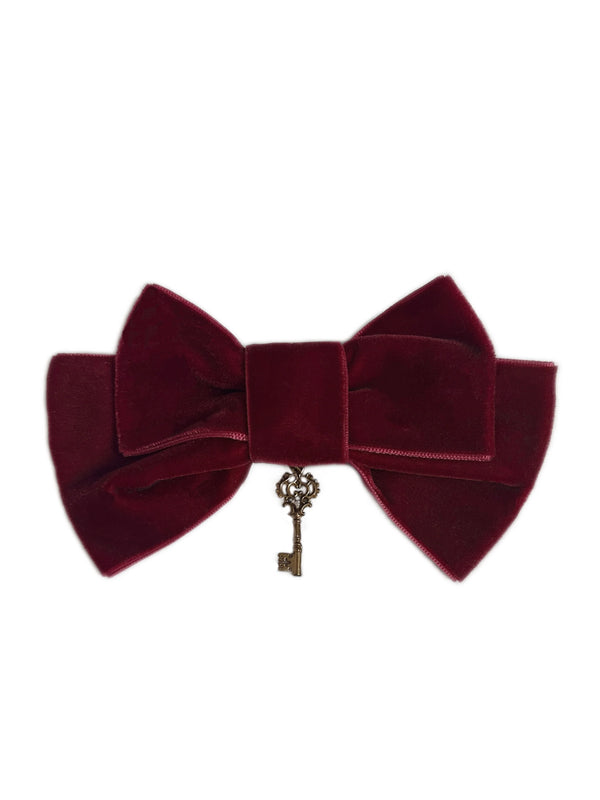 Burgundy bow accessory with a hanging key charm against a white background