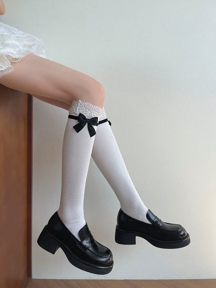 White lace-cuff slouch socks with black bows styled with polished black loafers.