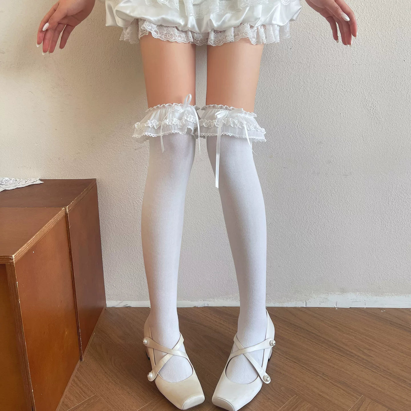 White thigh-high socks with layered lace ruffles and bows styled below a white ruffled skirt.