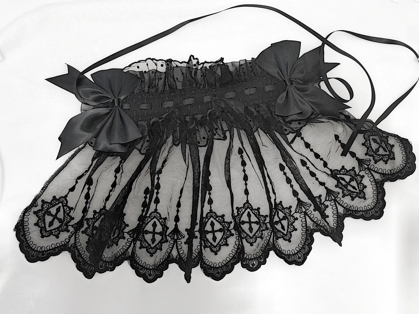 Black face-covering lace headband with large bows and trailing ribbons laid flat.