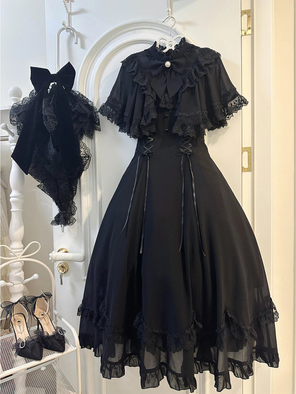 Black lace-cape OP dress with collar bow, side lacing and layered hem on a hanger.