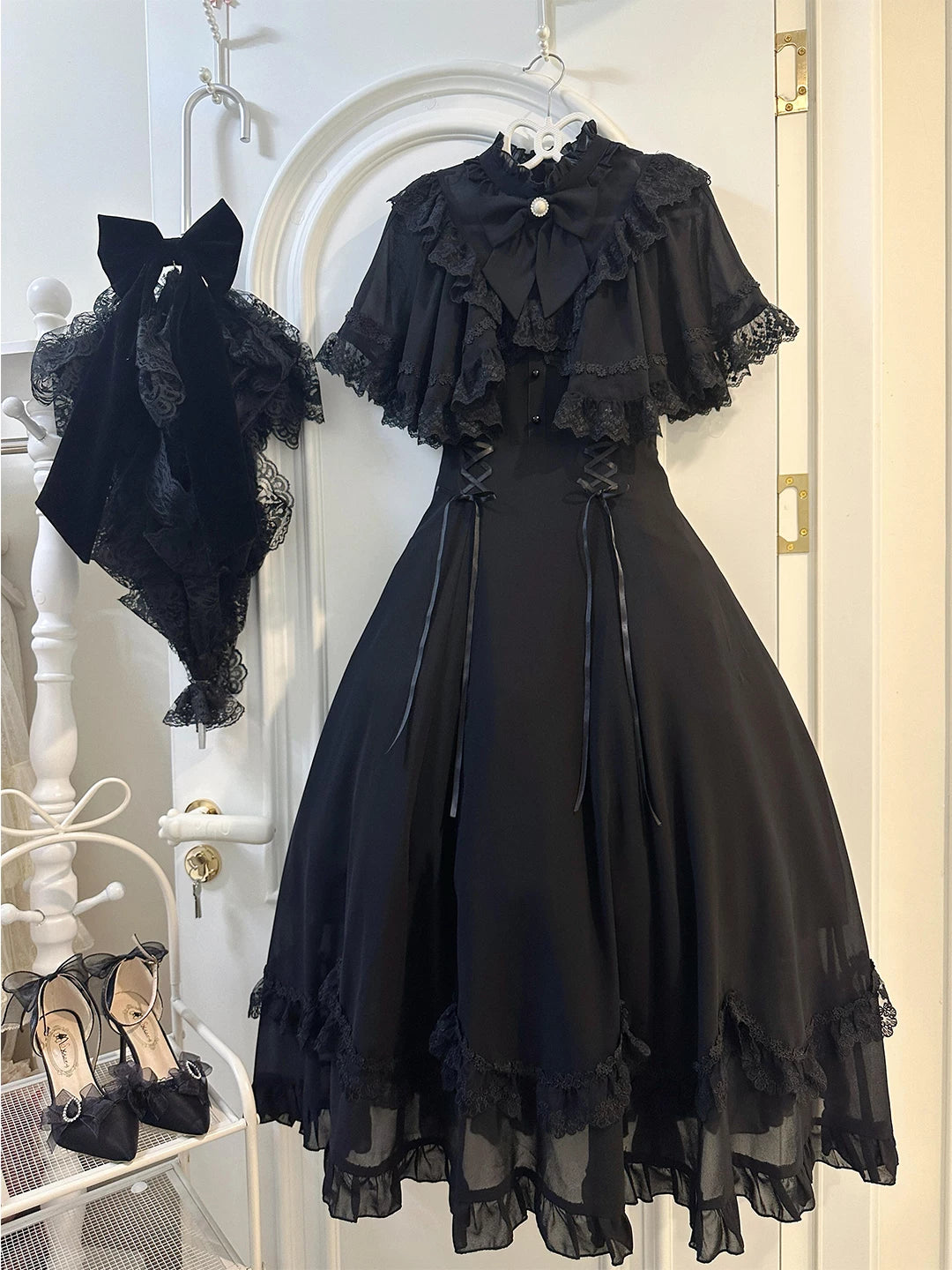 Black lace-cape OP dress with collar bow, side lacing and layered hem on a hanger.