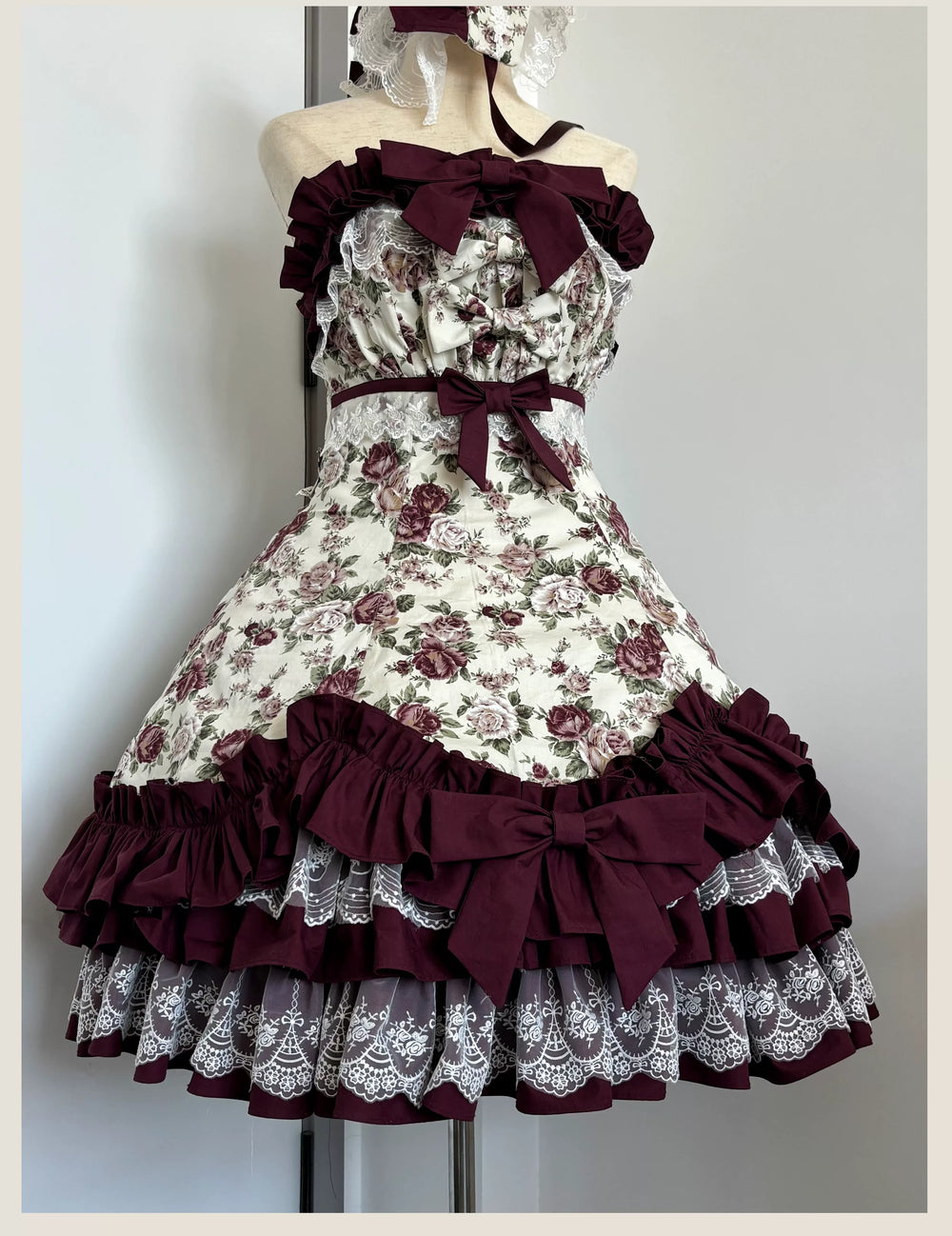 Burgundy and cream floral JSK dress with tiered ruffles, lace panels and oversized bows on a mannequin.