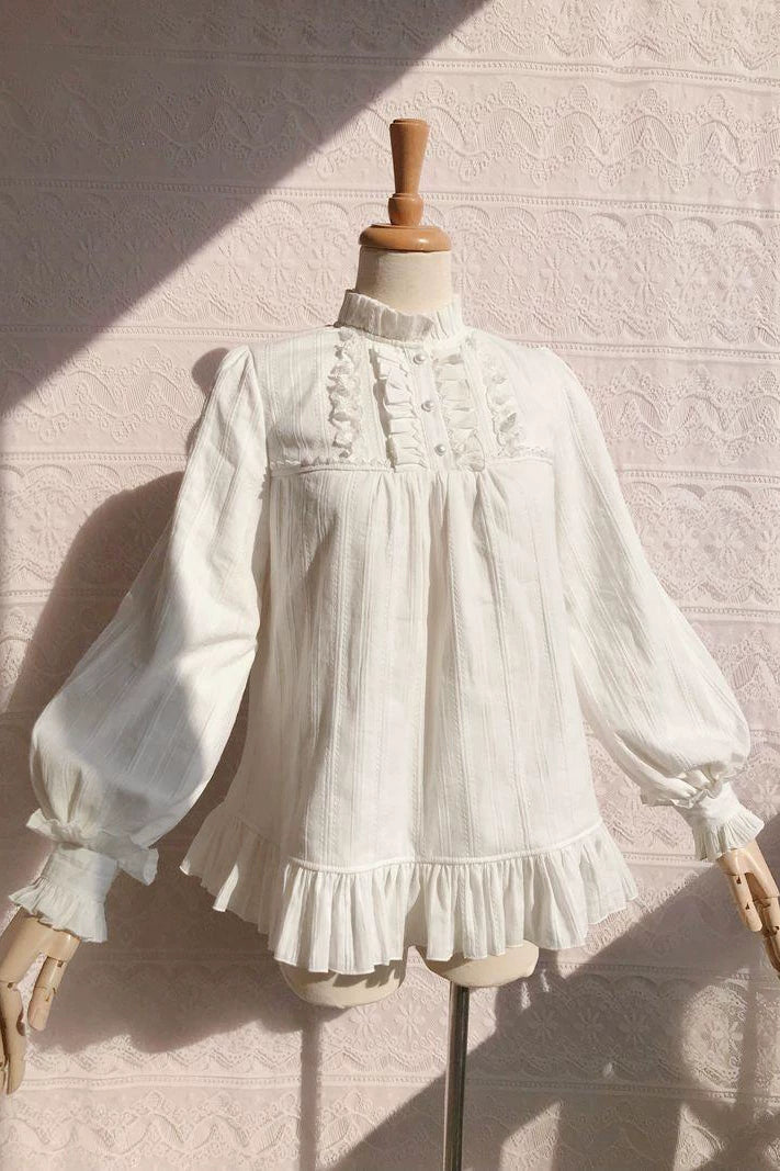 Off-white long-sleeve jacquard blouse with a ruffled collar and flounced hem on a mannequin.