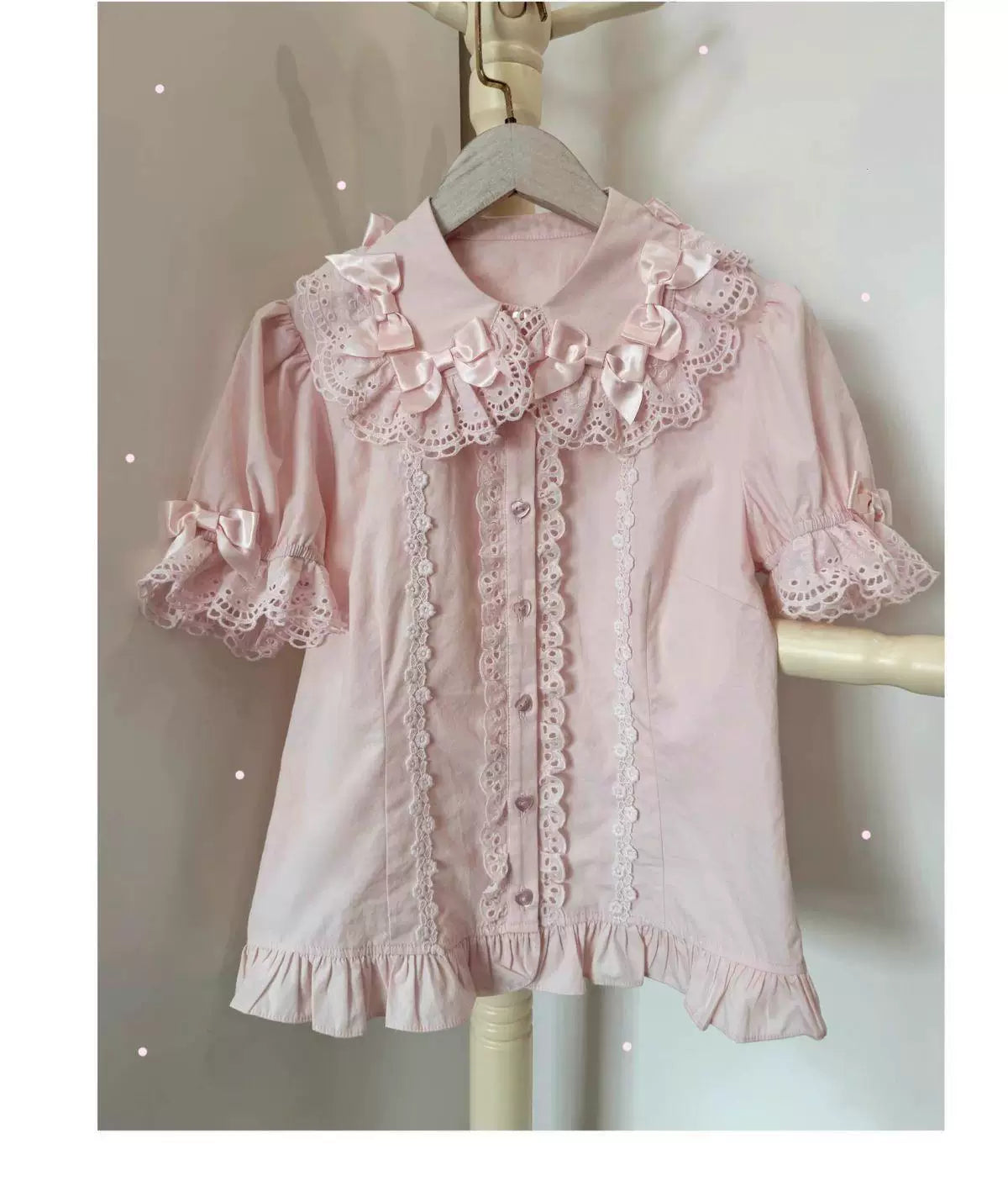 Pink short-sleeve blouse with a lace-trimmed doll collar, bows and ruffled hem on a hanger