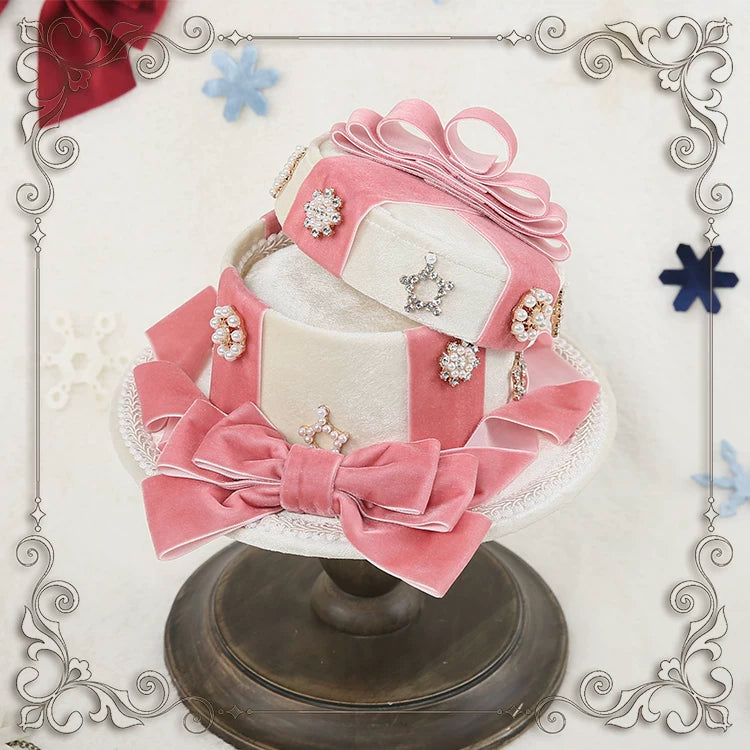 Pink-and-white velvet gift-box top hat with layered bows and jeweled accents on a display stand.