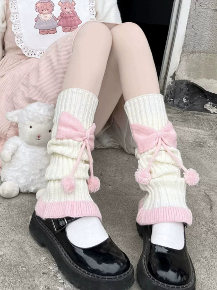 Pink-and-white ribbed leg warmers with large bows and dangling pom-poms styled with black platform Mary Janes.