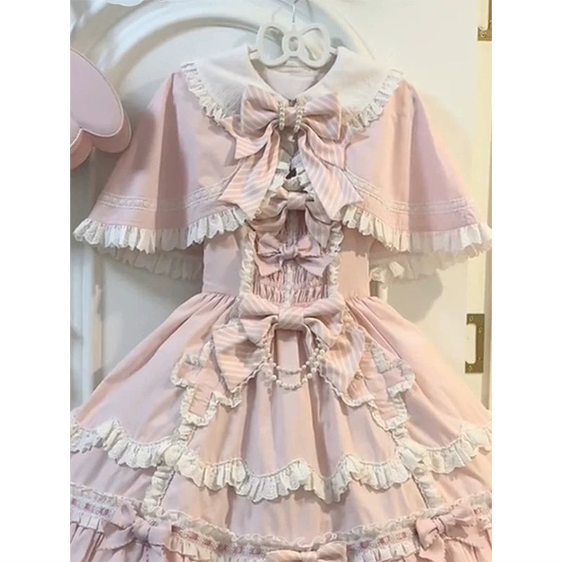 Pink Lolita JSK with matching cape and bow hanging on a door.