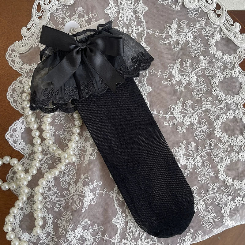 White mesh slouch socks with lace ruffles and bow cuffs styled with cream Mary Jane shoes.
