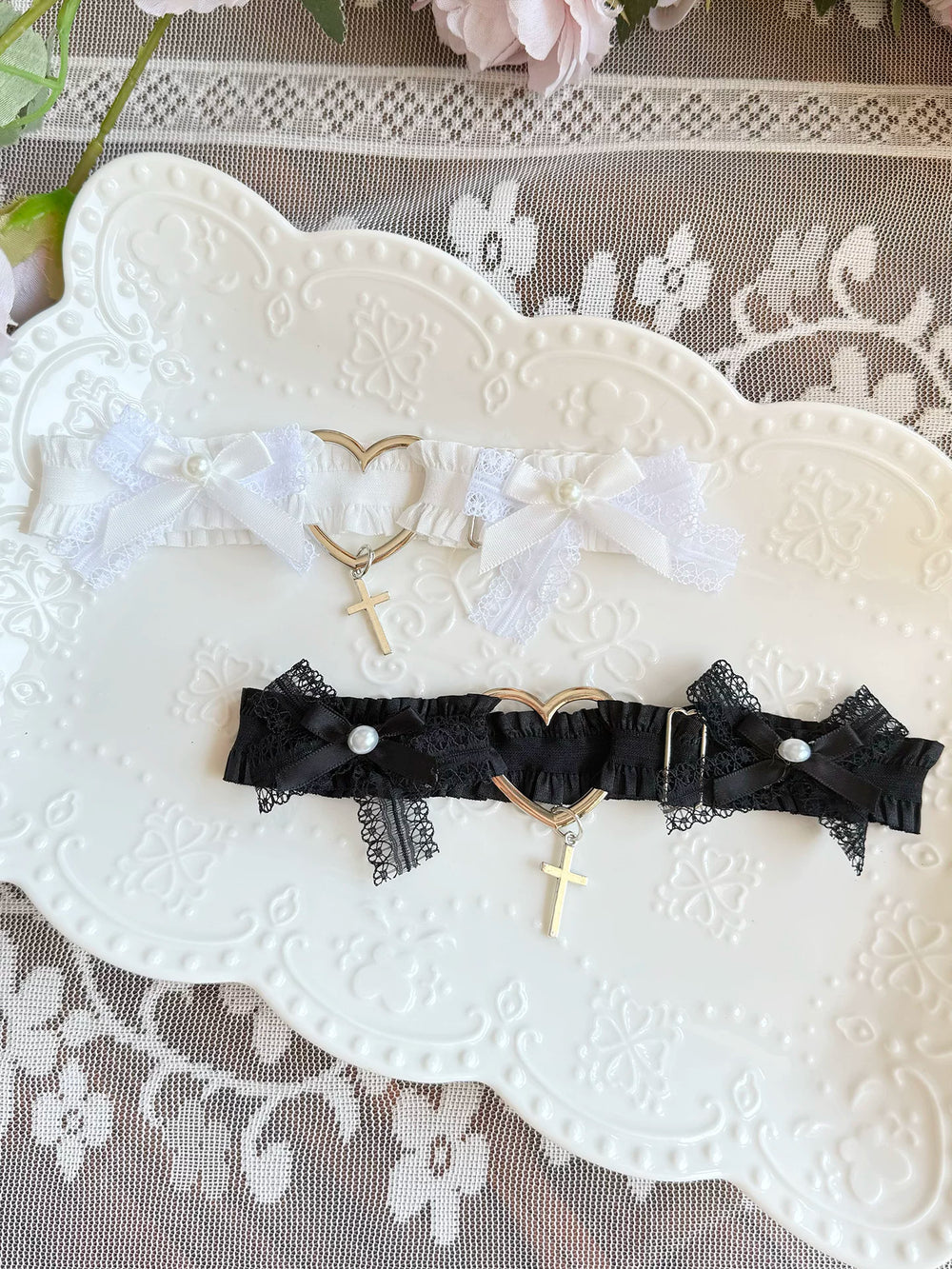 Black and white lace thigh garters with bows and heart-and-cross charms on a white embossed plate.