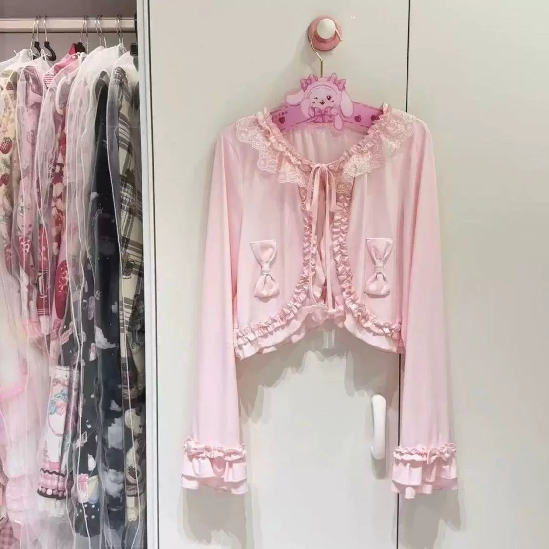 Sweetheart Dream Machine pink lace-trimmed bow cardigan shown on a hanger