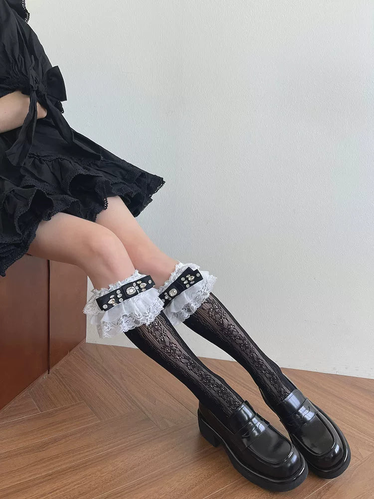Black lace mid-calf socks with white ruffled trim and jeweled bows styled with black loafers.