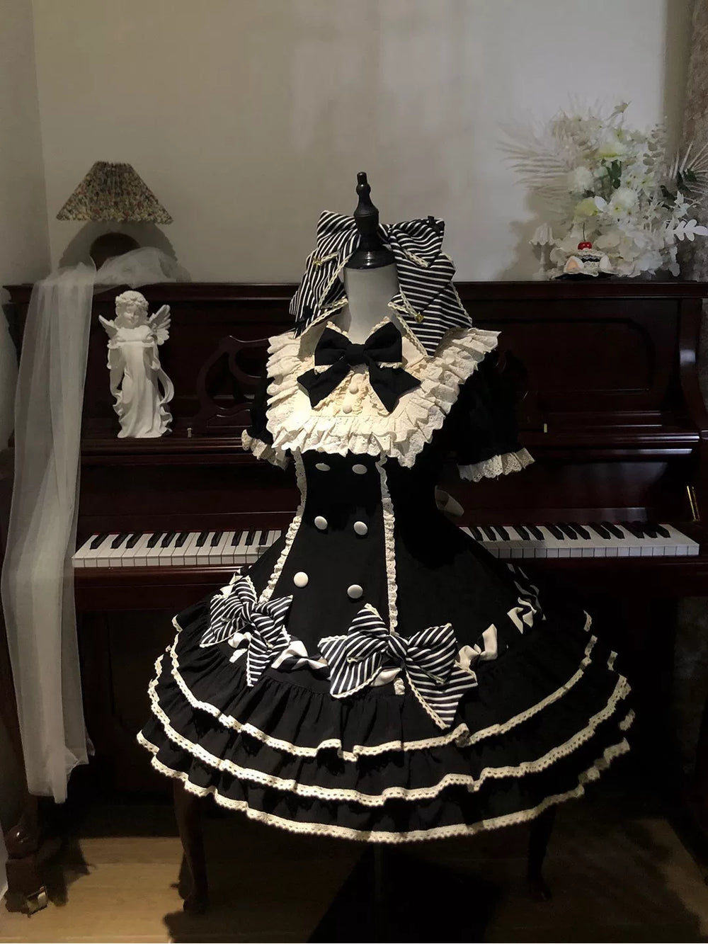 Black tiered Lolita dress with ivory ruffles and striped bows displayed on a mannequin.