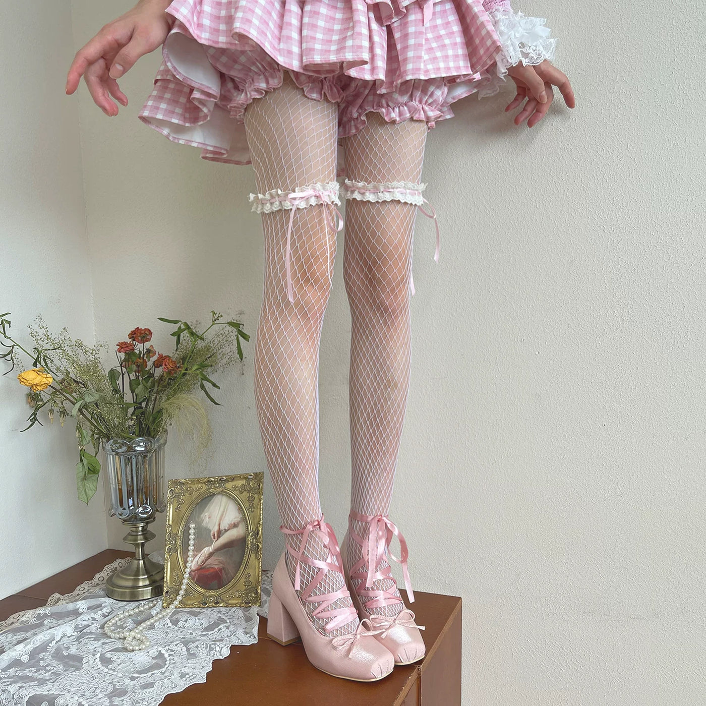 Pink fishnet Lolita pantyhose with lace bands and bows worn with pink heels