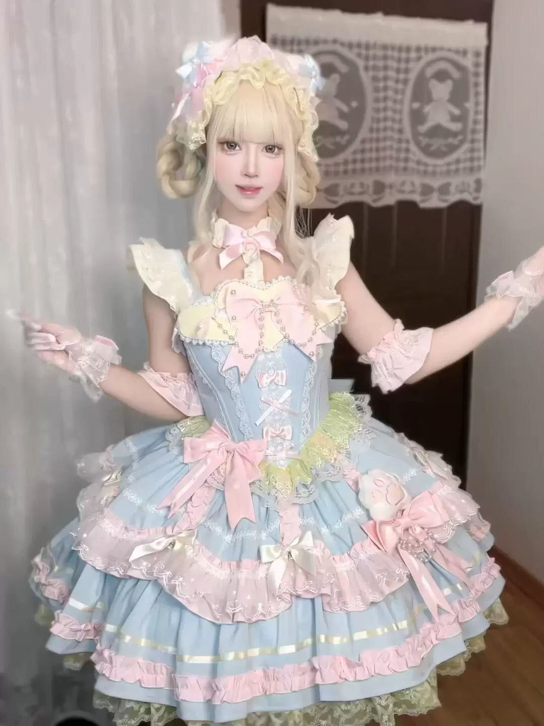Pastel blue-and-pink Sweet Lolita JSK with bows, layered ruffles, and train, worn by a model.