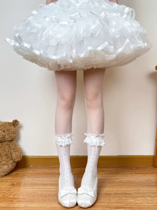 White openwork heart-pattern socks with lace ruffle cuffs and bows, worn with a white skirt.