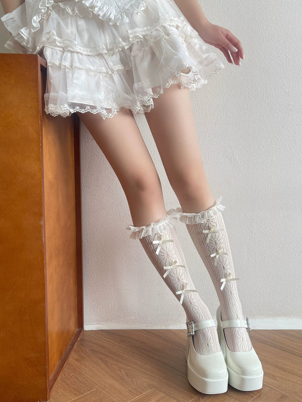 White lace calf socks with ruffled cuffs and small bows styled with white platform Mary Janes.