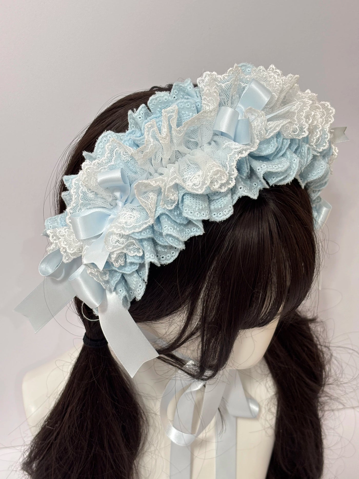 Blue and white lace hairband with layered bows and long ribbons shown on a mannequin.