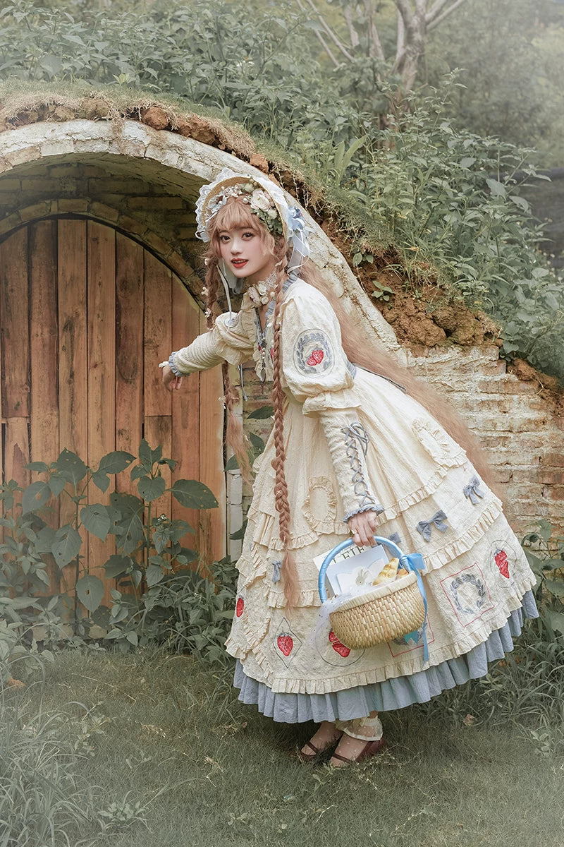 Cream long-sleeve Strawberry Jam OP with red strawberry motifs and blue-grey ruffles outdoors.