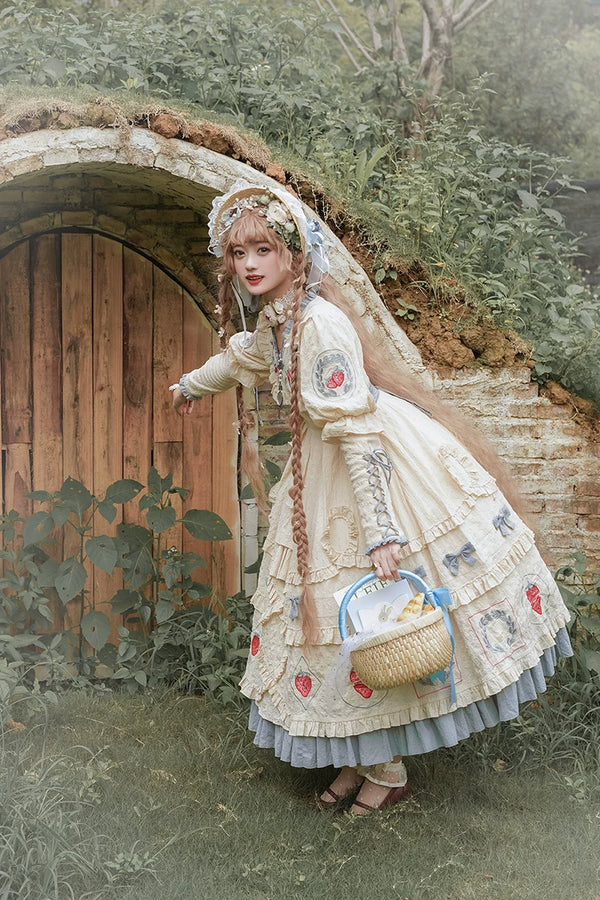 Cream long-sleeve Strawberry Jam OP with red strawberry motifs and blue-grey ruffles outdoors.
